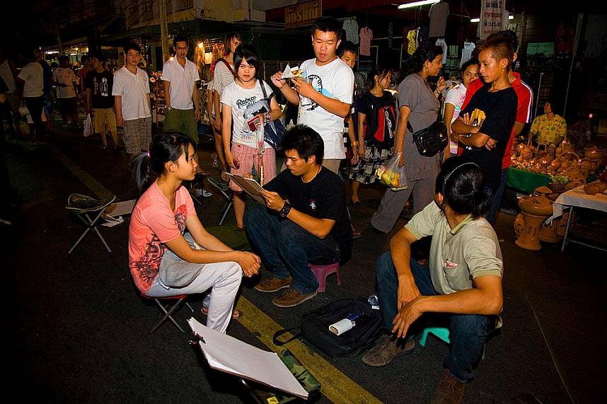 Young artists paint a picture of a tourist at Walking Street in Chiang Mai